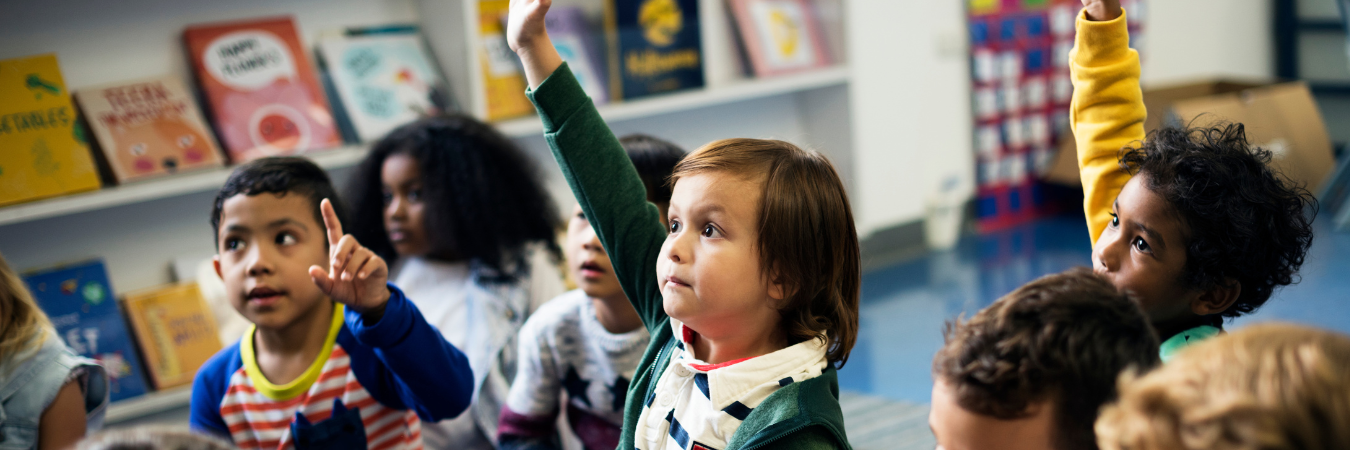 Class of small children with their hands raised