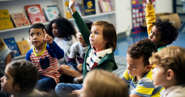 Class of small children with their hands raised