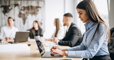 female worker in office suit on laptop with colleagues 