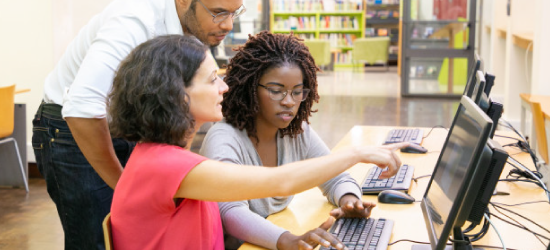 Two Women And a Man In Library Looking At Computer