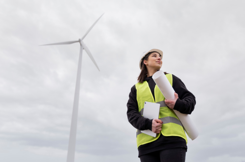 Female engineer wearing high vis standing in front of a wind turbine 